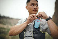 An athlete preparing for a run, holding a water bottle with a hydration tube, outdoors in a natural setting.