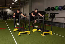Two men performing sled push exercises in a gym, focusing on strength and endurance training for runners.