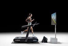 Woman running on a treadmill with virtual outdoor scenery on screen, showcasing indoor running and virtual training technology.