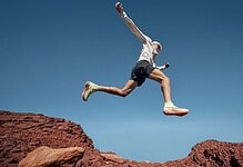 A trail runner in mid-air jump over rocky terrain during outdoor run, showcasing agility and endurance in nature.
