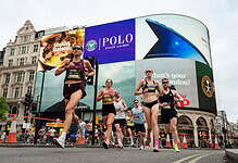 Group of runners participating in the London 10K race, with iconic Trafalgar Square buildings and digital advertising billboards in the background.