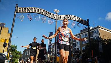 Female runner celebrating crossing the finish line at Hoxton Street Market during Saucony Run Shoreditch Half 2026 event.