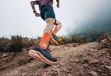 Runner in trail shoes and orange socks running on a rugged mountain trail with misty background.