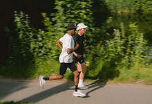 Two runners, a man and a woman, jogging along a scenic riverside path surrounded by lush greenery.